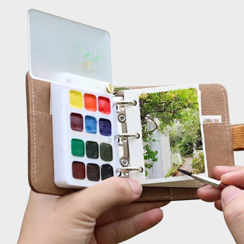 Open brown leather Nomad Mini Kit held in hand, painting a garden archway with the 12-color palette